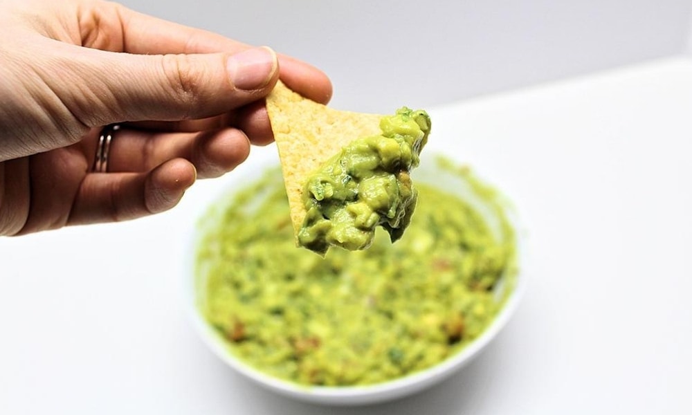 Hand holding up a chip covered with homemade guacamole.