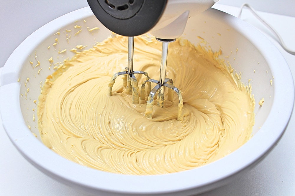 Electric hand mixer blending cream cheese and sweetened condensed milk.