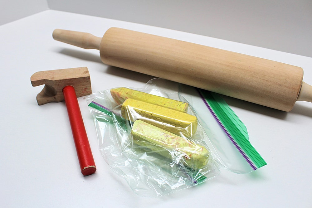 Bag containing yellow chalk, next to a rolling pin and toy hammer.