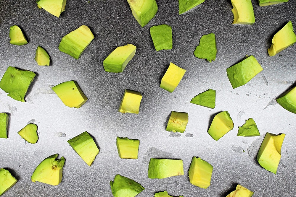 Pieces of avocado laid out on a baking sheet.