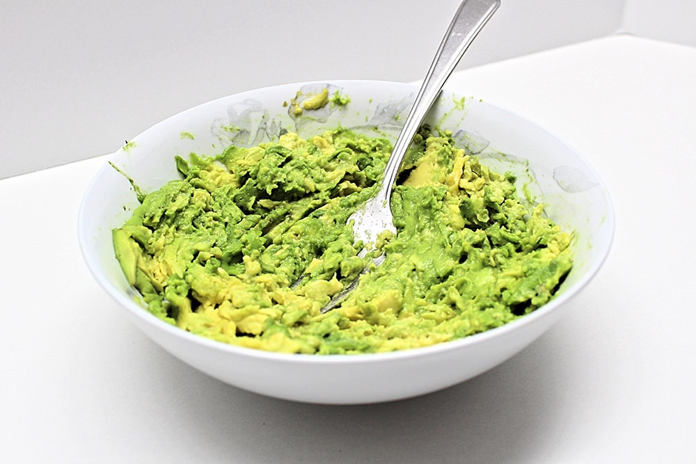 Bowl filled with avocado being mashed with a fork.
