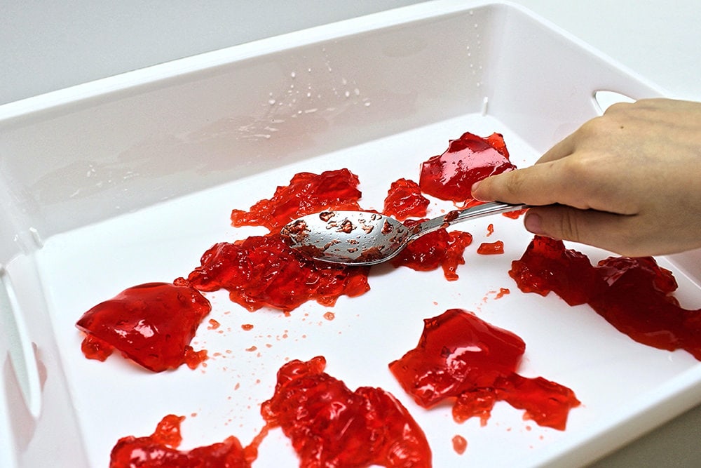 Child smashing red Jell-O with a spoon.
