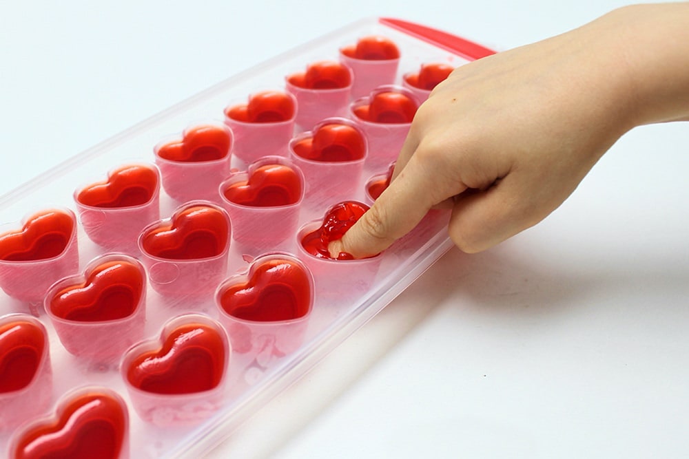 Child's finger pressing down on Jell-O placed inside a Valentine's Day ice cube tray.