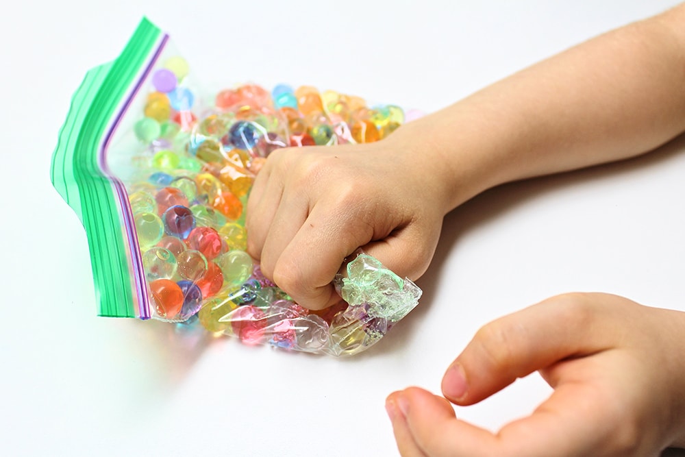 Child's hand squishing a bag filled with hydrated water beads.