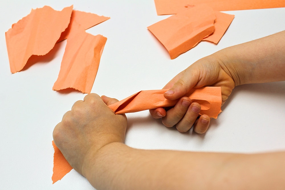 Child's hands tearing up orange construction paper.