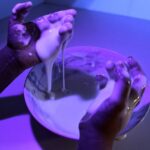 Child's hands playing with glowing slime in the dark.