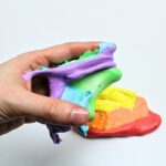 Hand holding up rainbow-coloured marshmallow slime.