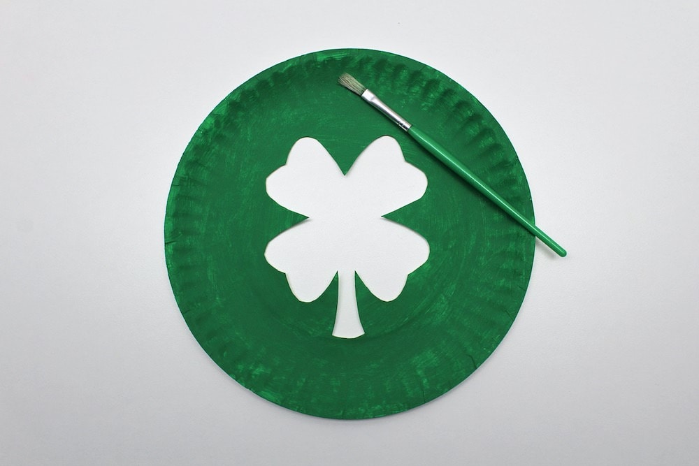 Paper plate painted green, with a clover shape cut out in the middle.