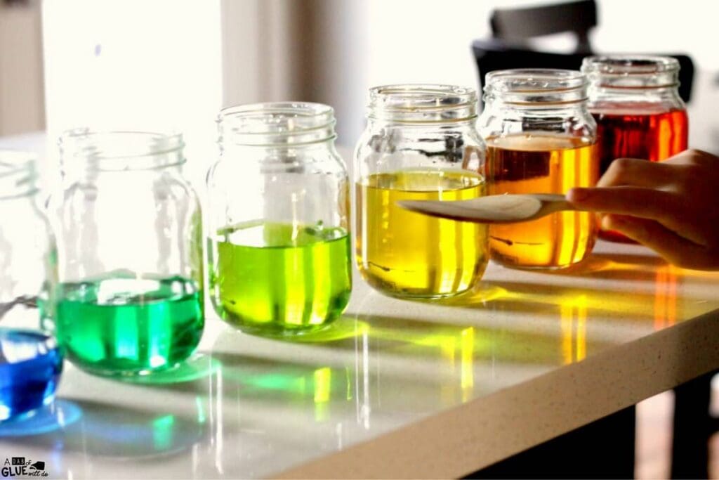 Rainbow lineup of glass jars containing coloured water.
