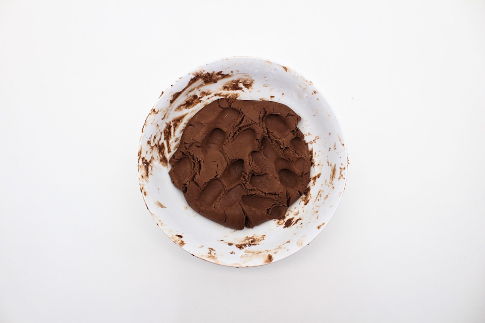 Chocolate play dough mixture kneaded inside bowl.