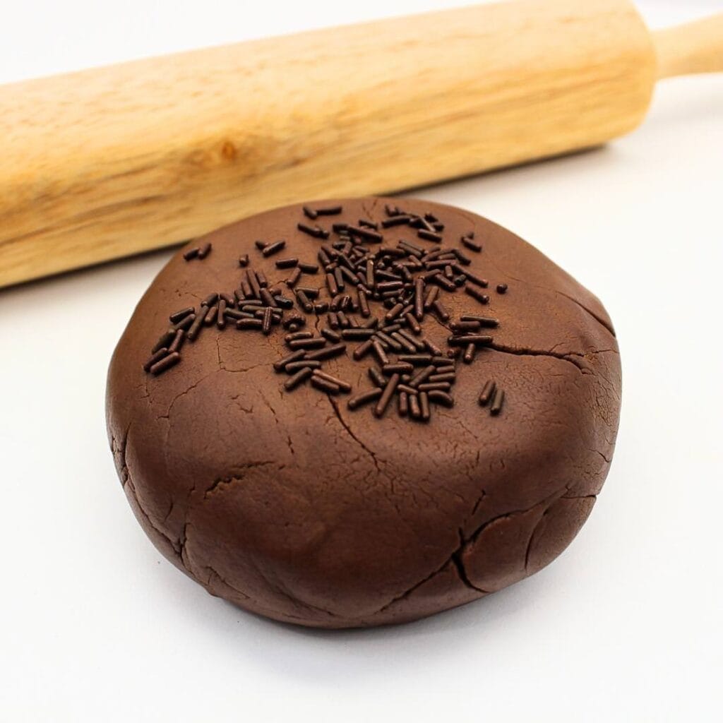Ball of edible chocolate play dough with chocolate sprinkles in front of rolling pin.