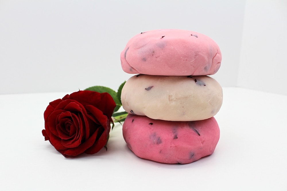 Stack of 3 balls of rose petal play dough beside a red rose