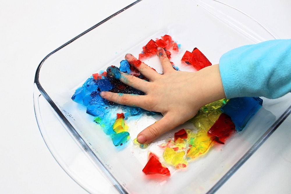 Child's hand squishing red, yellow and blue gelatin cubes.