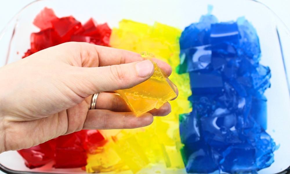 Hand holding yellow gelatin cube in front of red, yellow and blue gelatin cubes