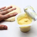 Hand squishing a ball play dough next to a pudding cup.