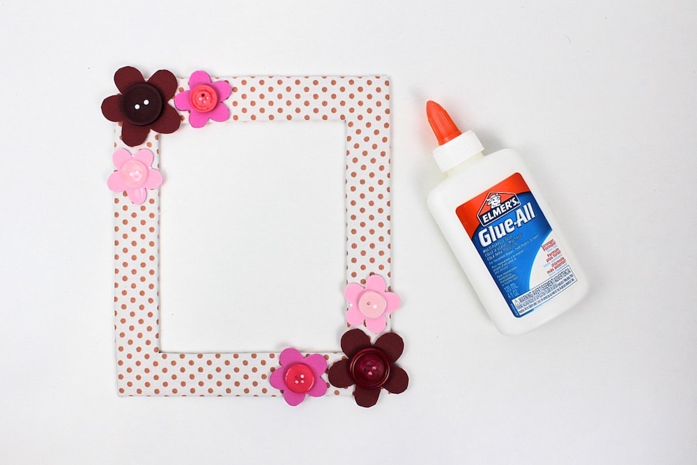 Frame with smaller flowers surrounding the larger ones next to bottle of glue.