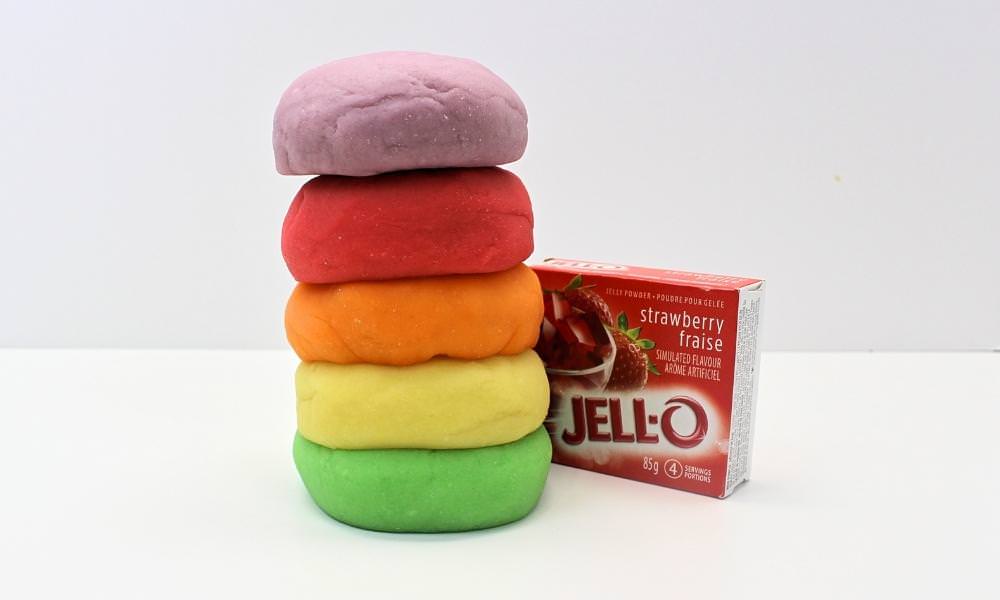 Stack of 5 colourful balls of play dough next to a box of strawberry Jell-O