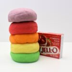 Stack of 5 colourful balls of play dough next to a box of strawberry Jell-O.