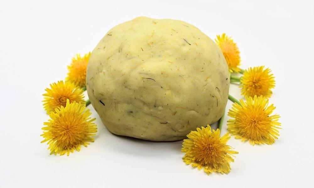 Ball of dandelion play dough surrounded by yellow dandelion flowers