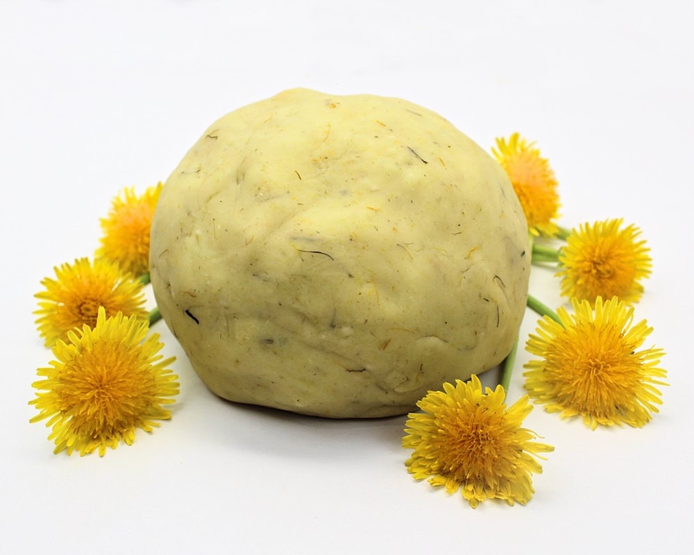 Ball of dandelion play dough surrounded by yellow dandelion flowers.
