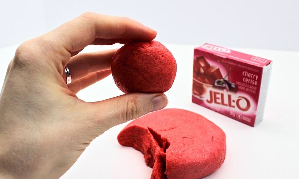 Hand holding round ball of Jell-O play dough in front of Jell-O box