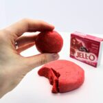 Hand holding round ball of Jell-O play dough in front of Jell-O box.