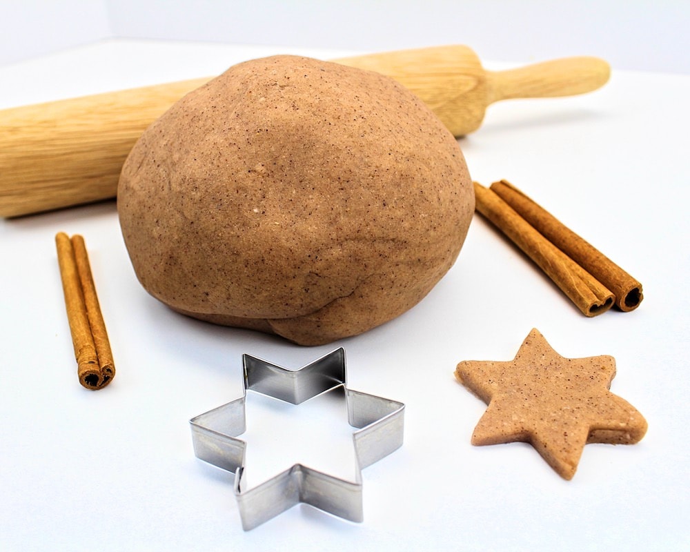 Ball of cinnamon-vanilla play dough with cookie cutter, rolling pin and cinnamon sticks.