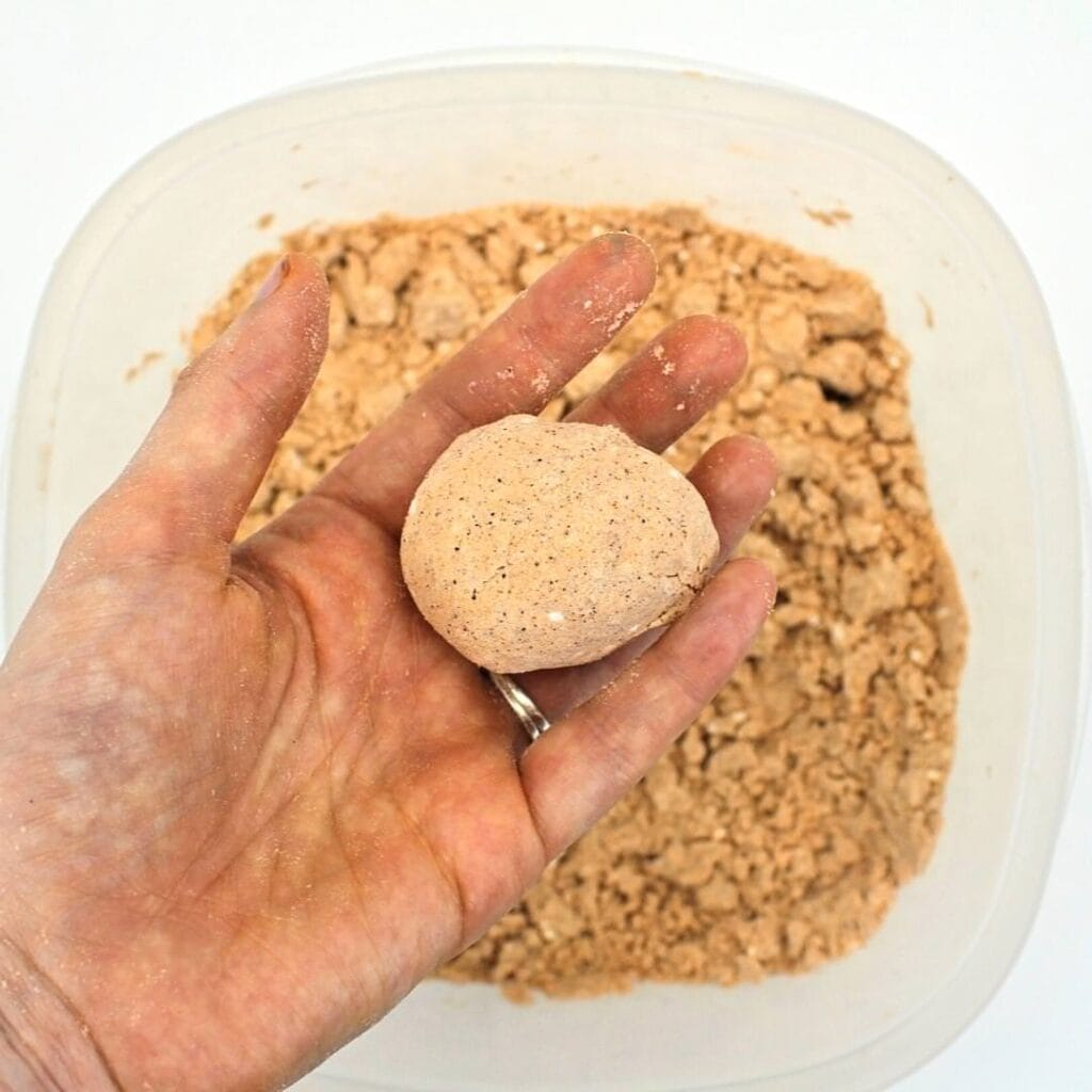 Hand holding ball of orange fall-scented moon sand.
