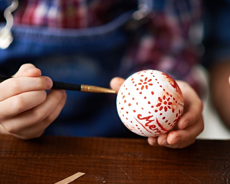 Child's hands painting a pattern on a Christmas ornament.