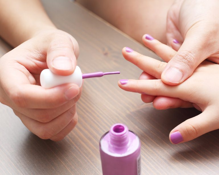 Adult's hands putting pink nail polish on child's nails.