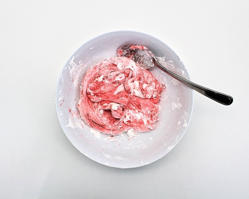 Red marshmallow fluff slime mixture stirred with spoon.