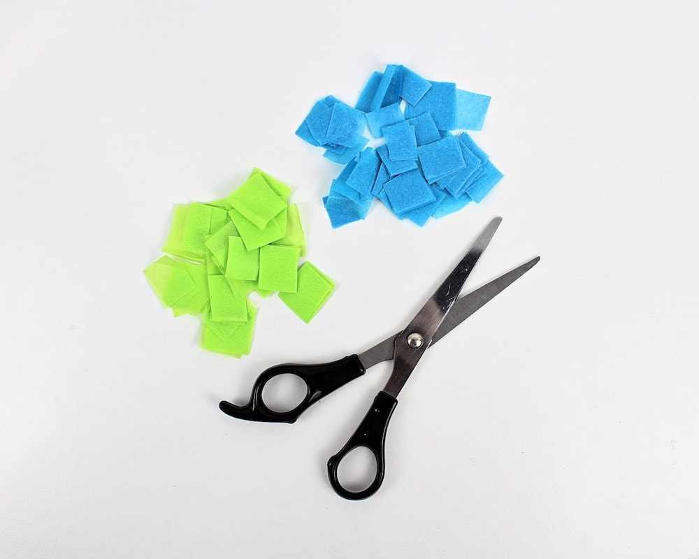 Scissors next to blue and green tissue paper squares.