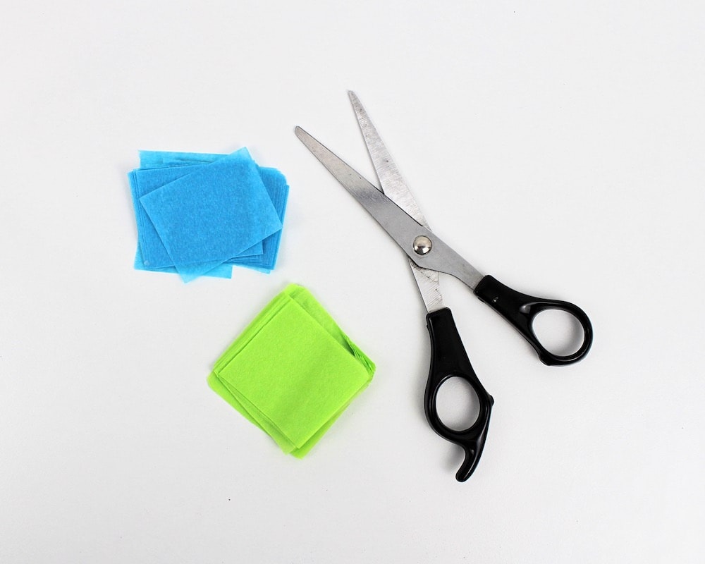 Scissors cutting blue and green tissue paper squares.