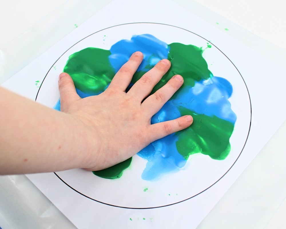 Child's hand smushing green and blue paint inside a bag.