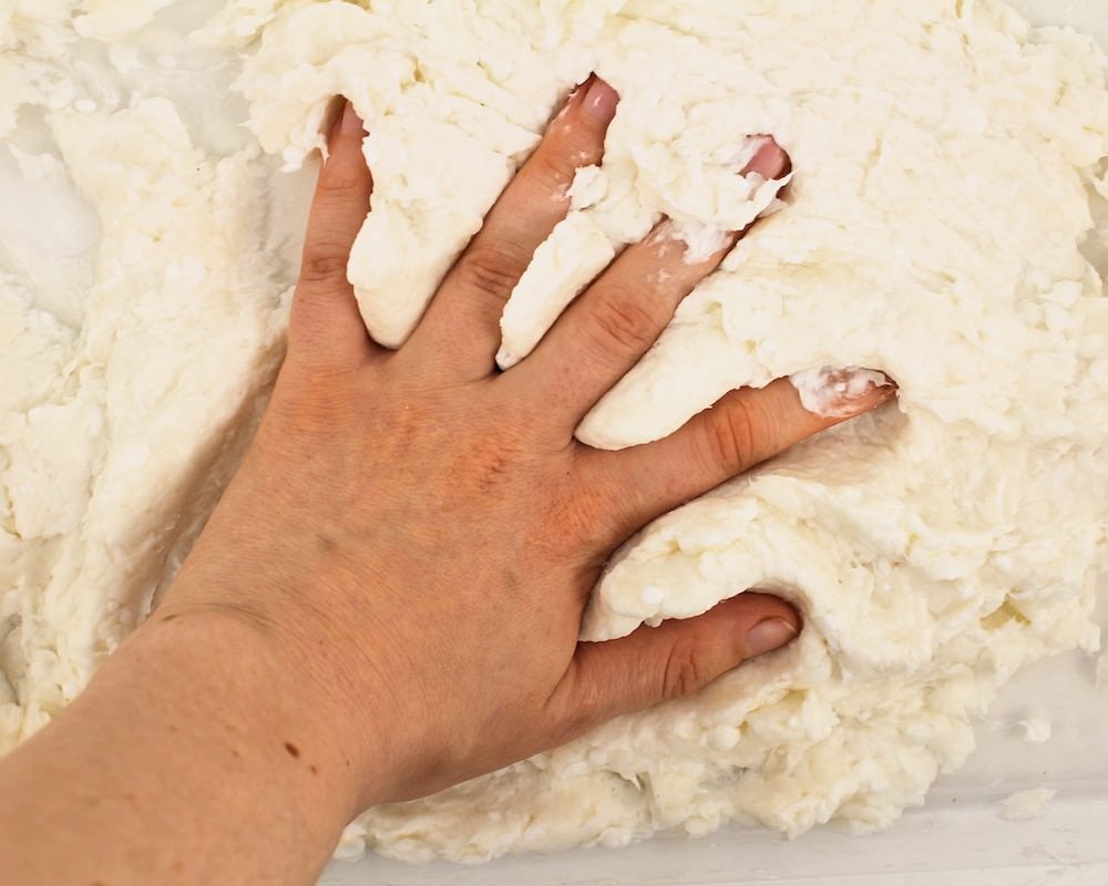 Hand pressing down into white dough.