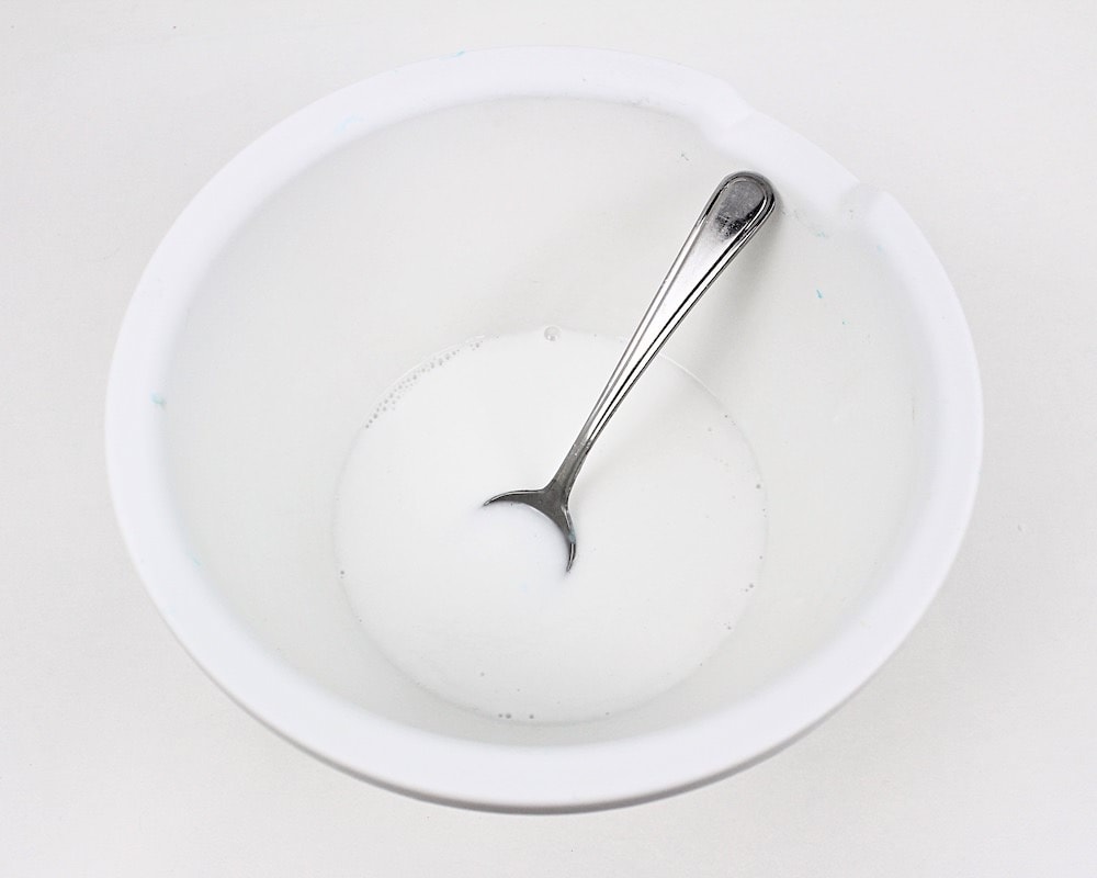 White bowl with white glue and water being stirred with a spoon.