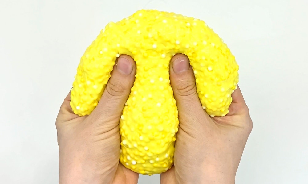Hands squeezing a ball of crunchy slime with foam beads