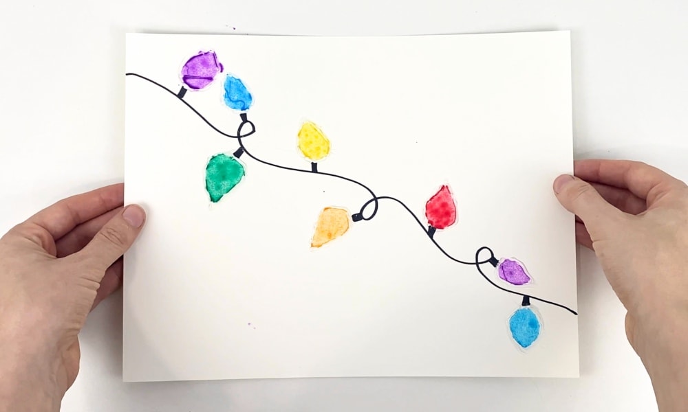 Hands holding up a Christmas lights craft made with hot glue and watercolour paint