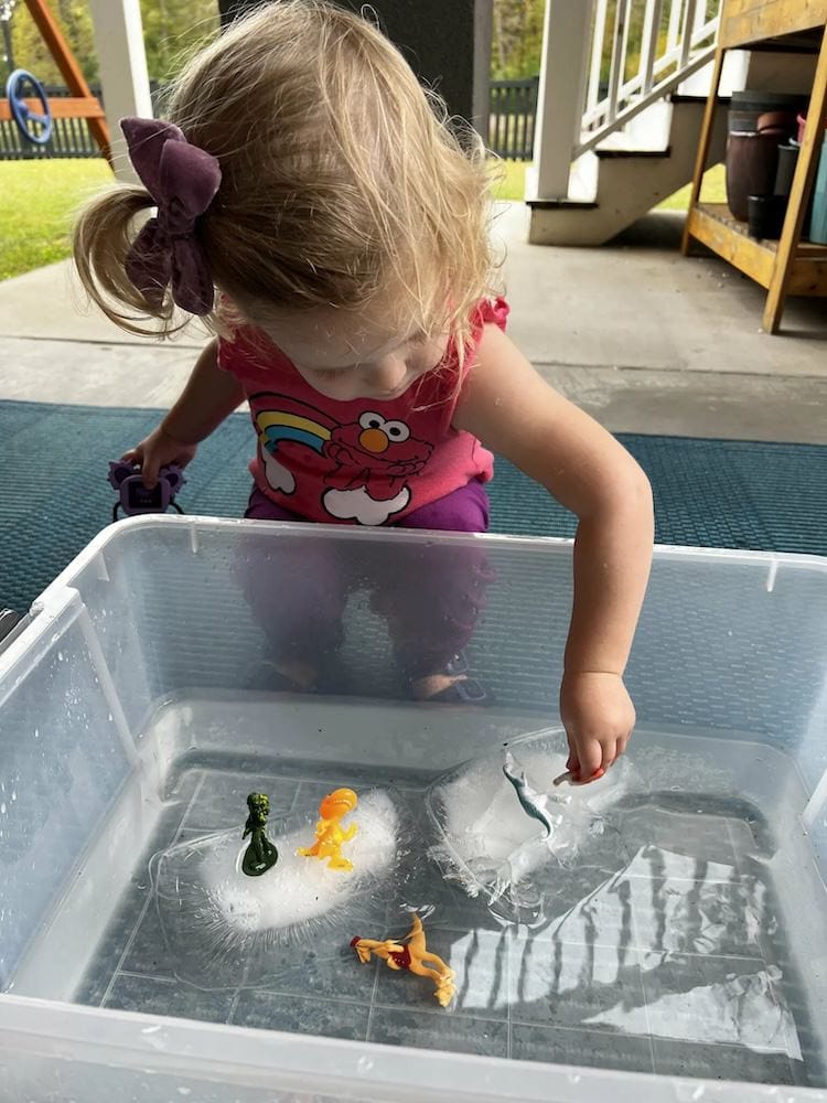 Girl playing in a bin filled with water, ice and plastic toys.