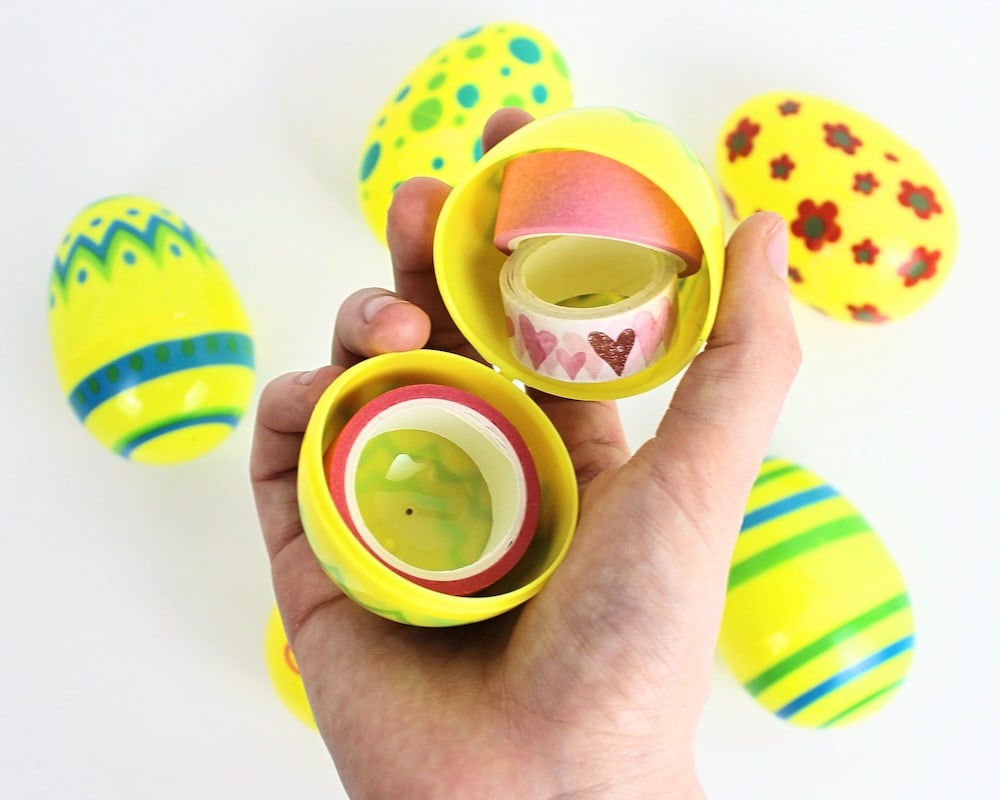 Hand holding up a yellow egg containing 3 rolls of washi tape, with more yellow eggs in the background.