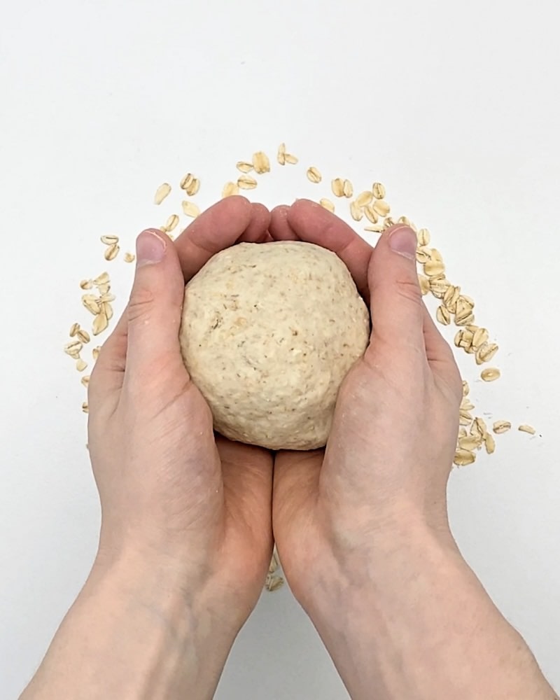 Hands cupping a ball of oatmeal play dough, with rolled oats underneath.