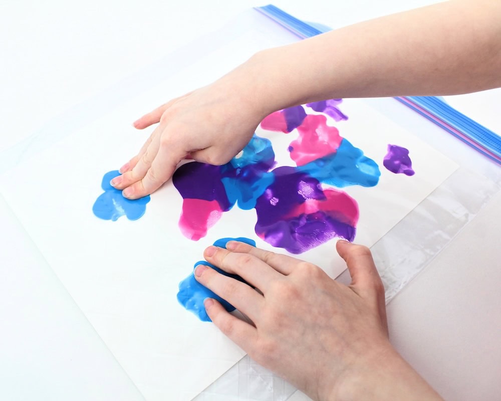 Child's hands smushing paint around inside a Ziploc bag.