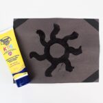 Sunscreen painting on black paper, next to a bottle of sunscreen.