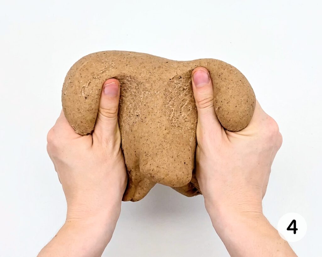 Hands kneading a ball of brown play dough.