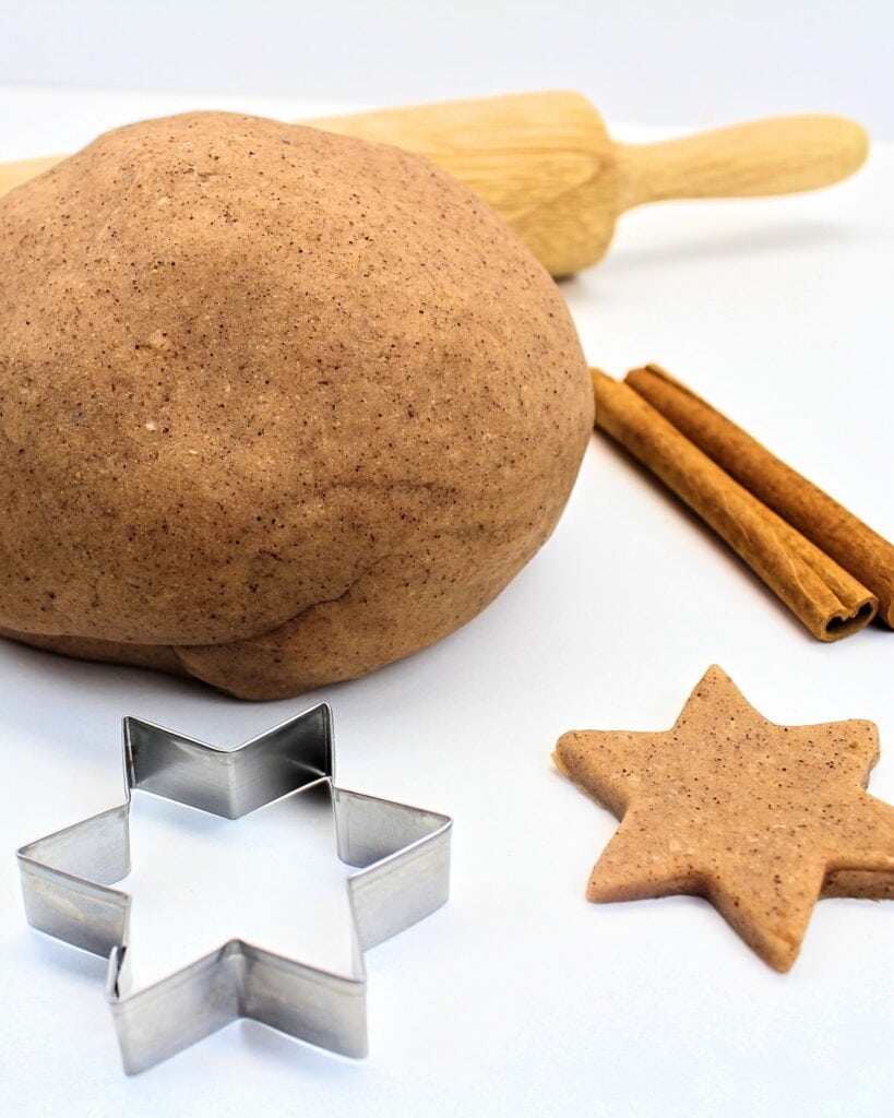 Ball of cinnamon-vanilla play dough with cookie cutter, rolling pin and cinnamon sticks.
