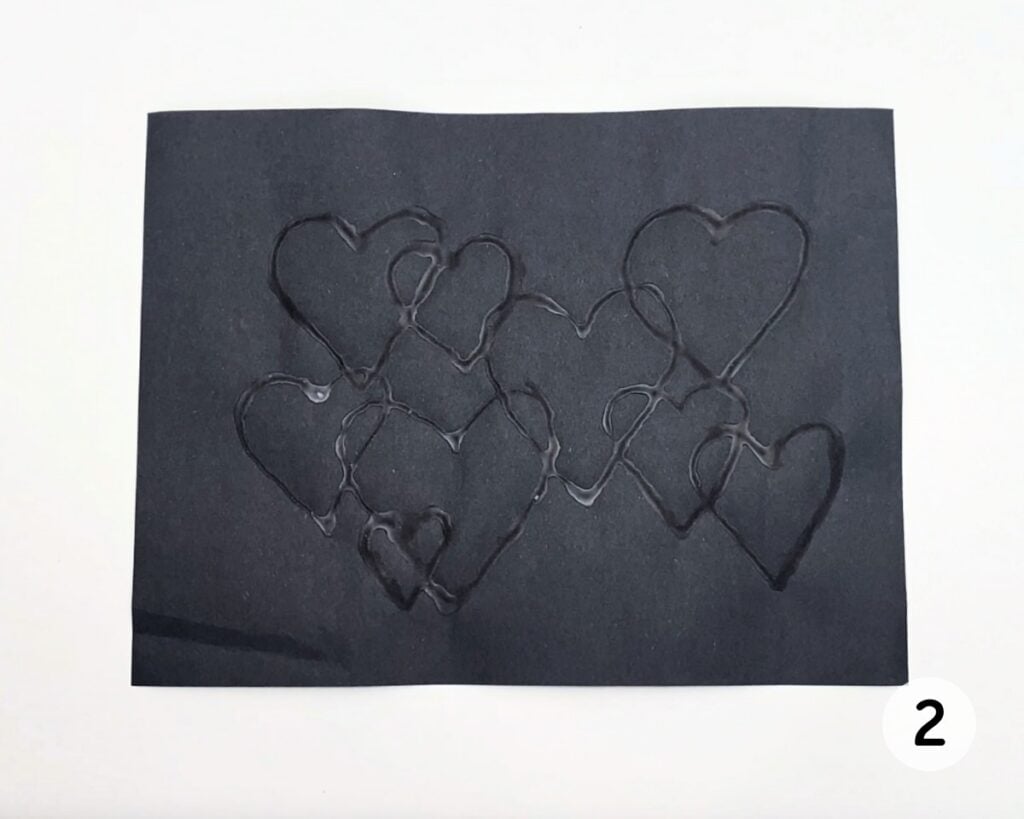 Overlapping hearts on black paper after glue has dried transparent.