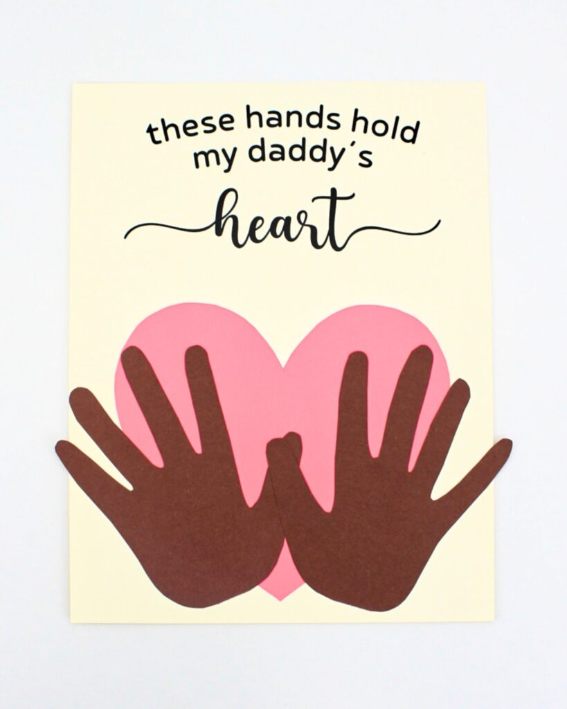 Father's Day craft with dark brown hands holding a pink heart.