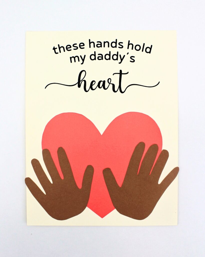 Father's Day craft with brown hands holding a light pink heart.