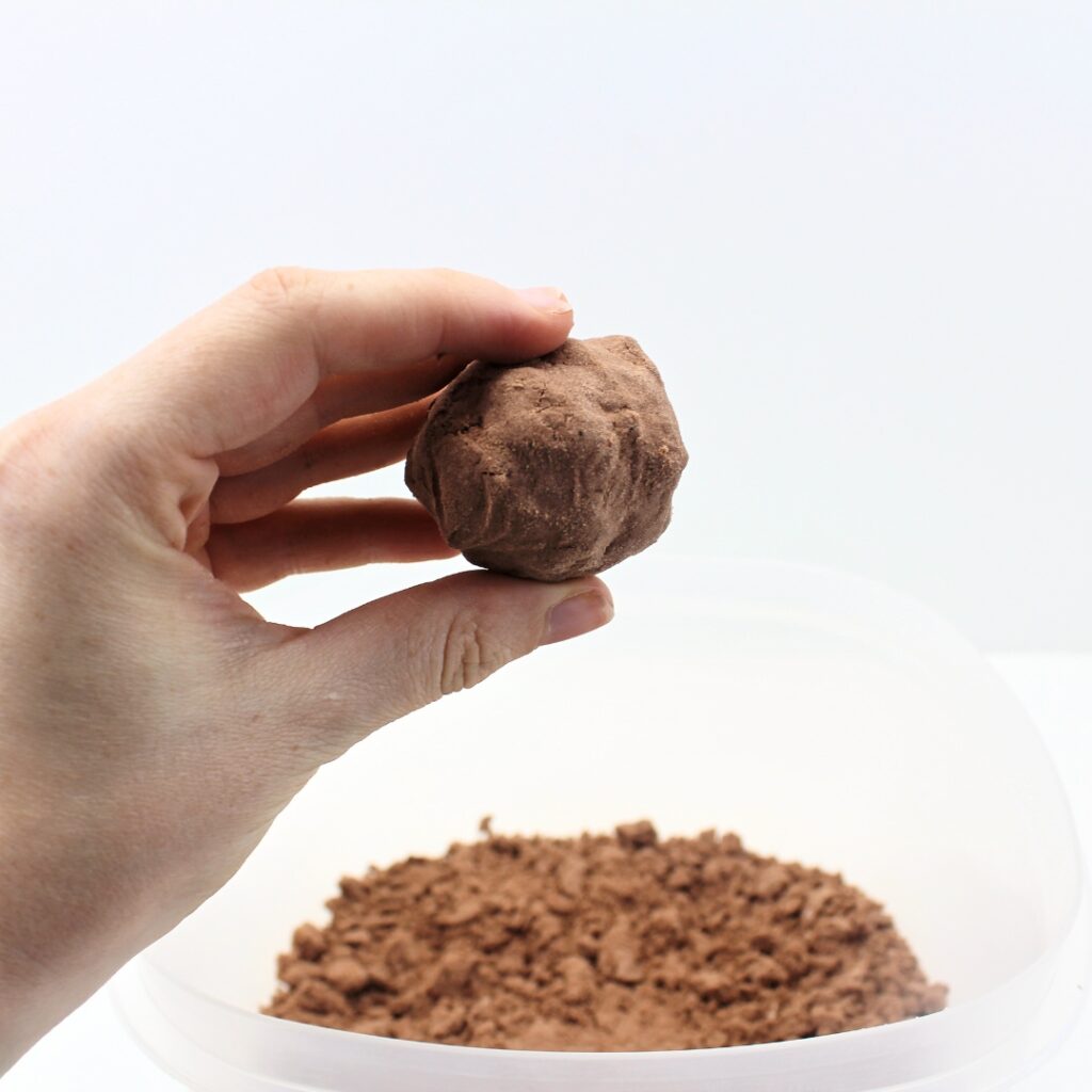 Hand holding up a ball of brown sand.