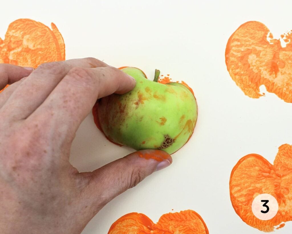 Hand pressing a painted apple onto cardstock.